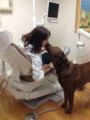 Patient in a dental chair kissing a dog