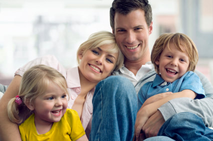 A family of two adults and two young kids posing and smiling for a family photo
